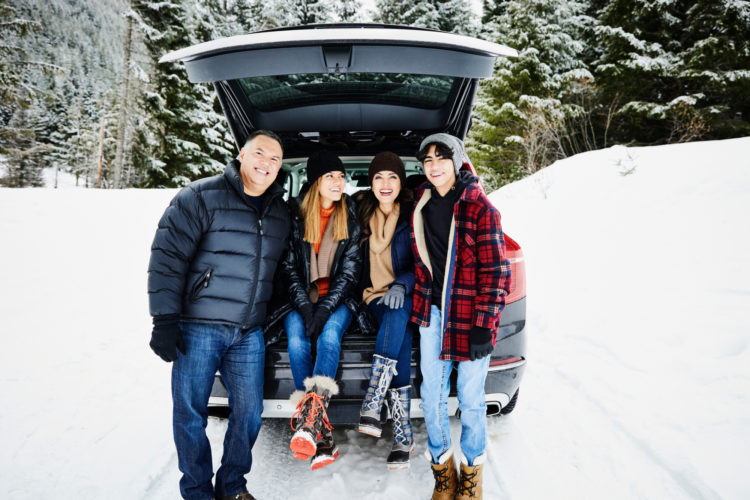 Family of four sitting in the truck of a car, posing for a picture on a snowy day